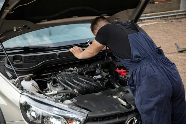 Mechanic checking car engine outdoors, focusing on vehicle maintenance and repair.
